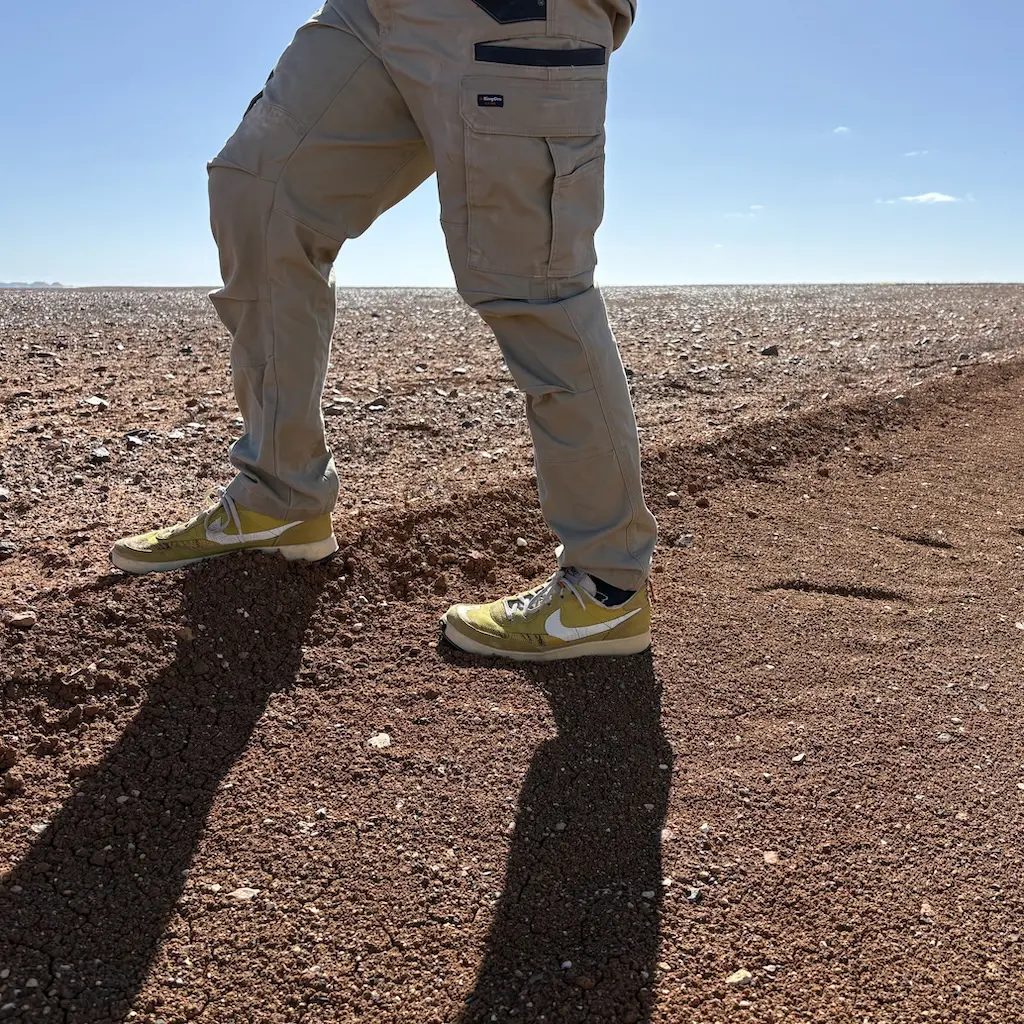 A photo of legs wearing Nike, General Purpose Shoes - archive colorway - stepping out onto the red matian like surface of the breakaways near Coober Pedy.