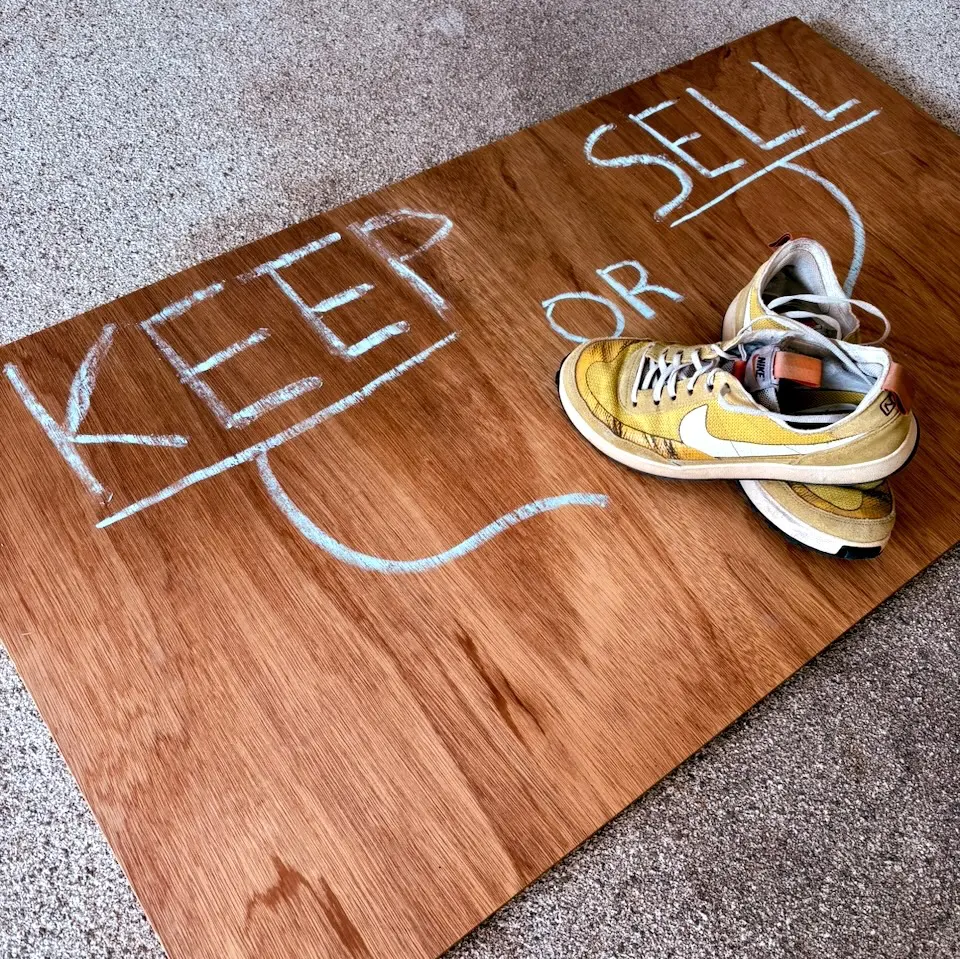 A photo of a pair of sulphur colored general purpose shoes resting on a sheet of plywood. The plywood has buy or sell written on it in chalk.