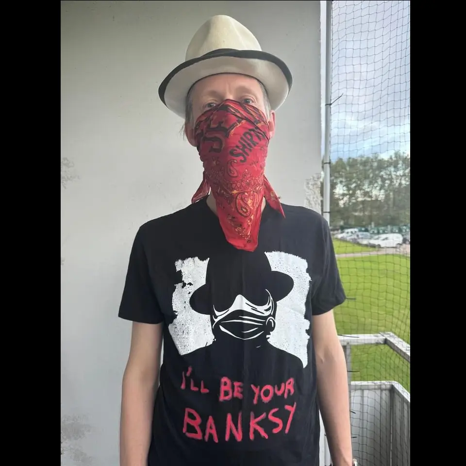 A photo of Anders wearing a red balaclava and the black I’ll Be Your Banksy t-shirt.